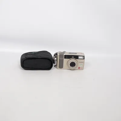 Analog kompaktkamera (Konica Z-up 130e, en analog kompaktkamera för 35 mm-film med en guldfärgad finish och ett inbyggt zoomobjektiv på 38–130 mm.Objektiv: Konica Lens 38–130 mm (f/4.1–13)Zoom: 3,4x optisk zoomFilmformat: 135-film (standard 35 mm)Autofokus: IR-aktiv autofokusBlixt: Inbyggd blixtBatteri: 1 st CR2 3V litiumbatteri    ) från Konica