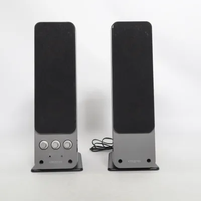Enceinte (aktiva 2.0-datorhögtalare av modellen Creative GigaWorks T20 Series II, utrustade med fysiska reglage för bas, diskant och volym på den vänstra enheten.Modell: Creative GigaWorks T20 Series II (2.0-system)Funktioner: Inbyggda rattar för bas, diskant och volym, samt uttag för hörlurar och aux-ingång på framsidan.) de Creative